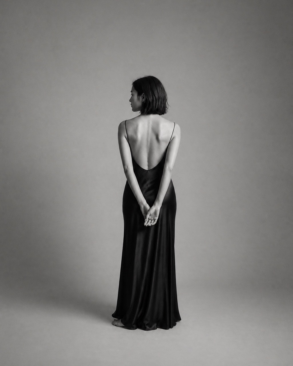 Black-and-white back view of a woman in a floor-length satin slip dress cut low across the back.