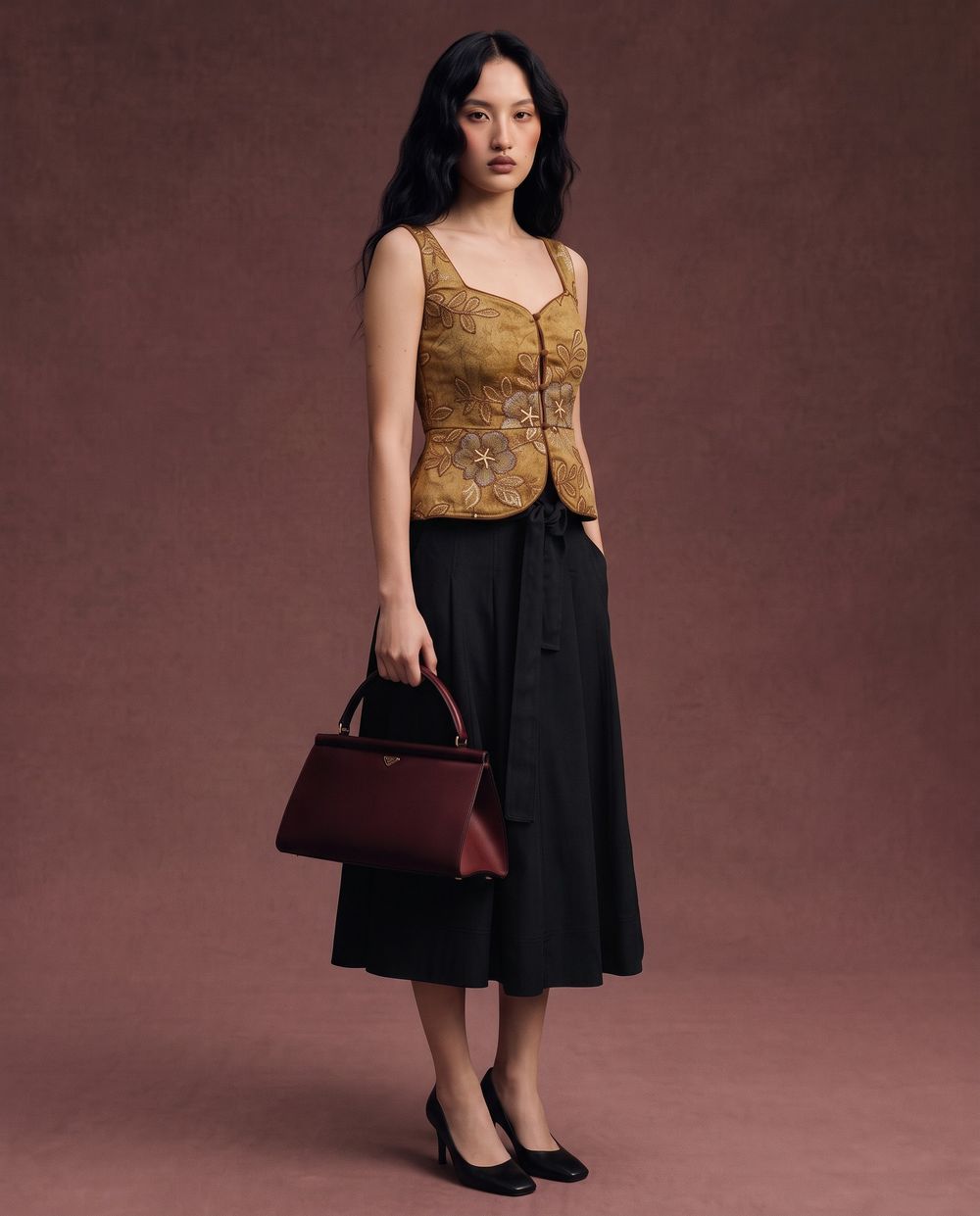 The same top styled with a black skirt and a burgundy bag on a deep maroon ground.