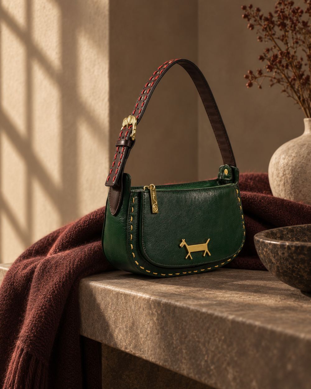 The green bag on a stone ledge beside a pale ceramic vase and a speckled bowl, window light across the wall.