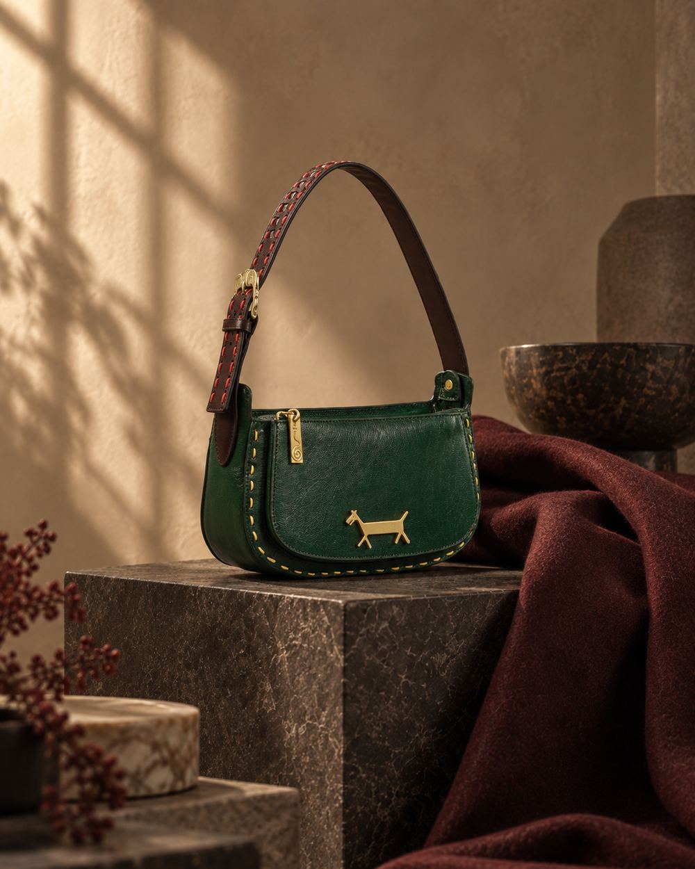 The green leather bag alone on a dark stone block, a maroon wool throw falling behind it.