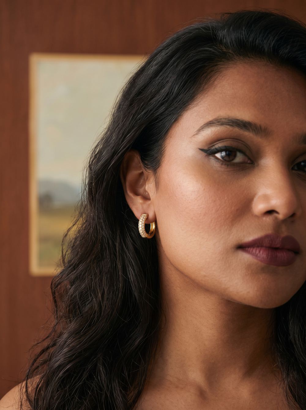 Close beauty portrait with a gold hoop in a warm interior.