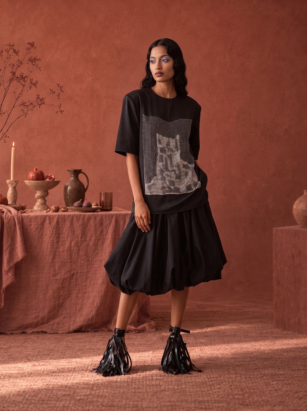 Full-length black tee and bubble skirt among candles and pottery.