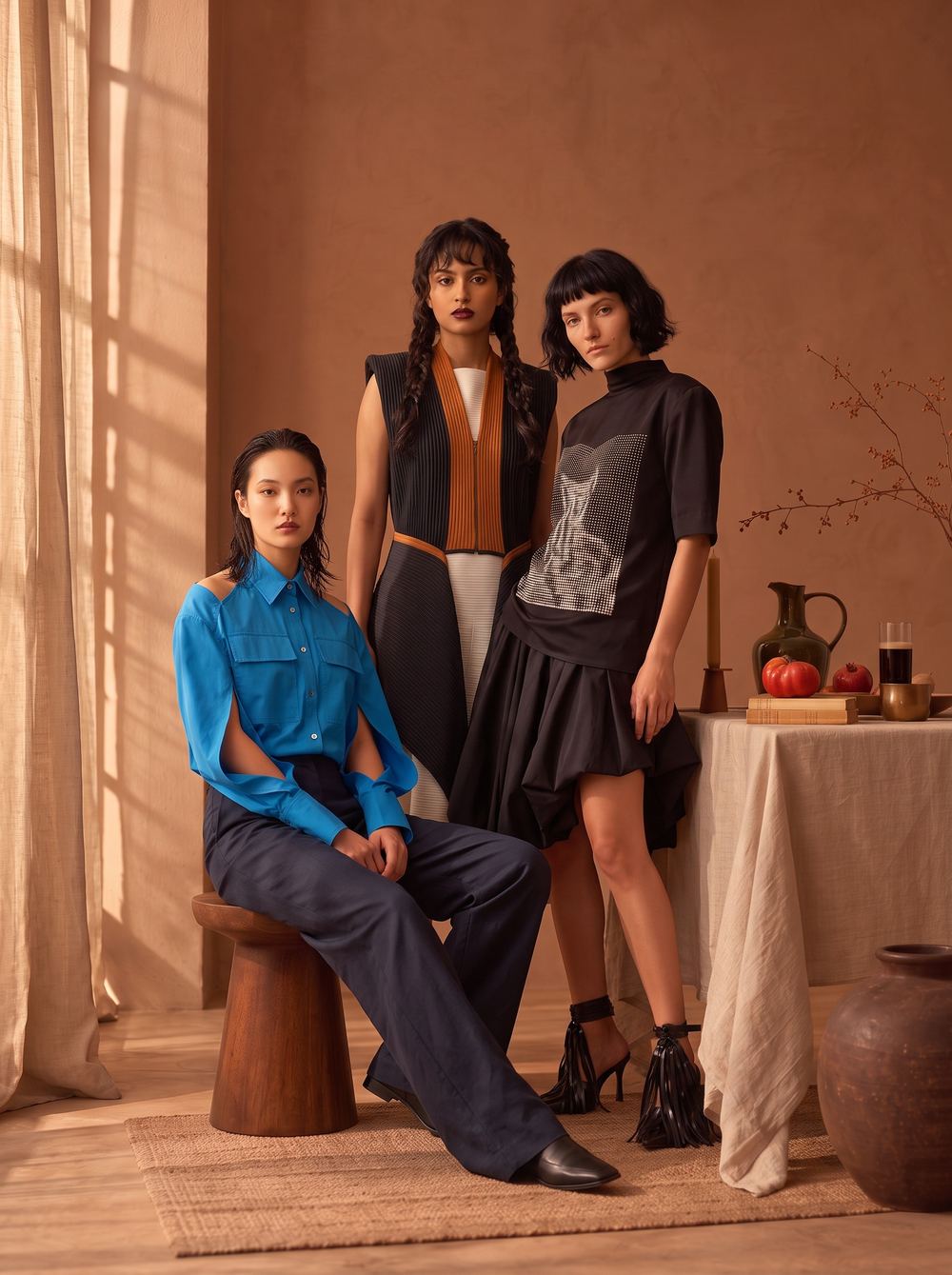 Four models in one collection — blue shirt, black skirt and tan waistcoat — in a warm room.
