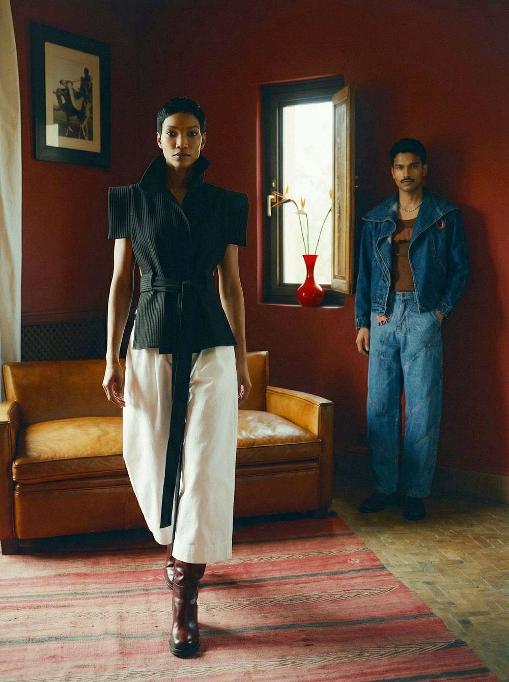 Red-walled room, the black vest and white skirt walking, a denim figure behind.