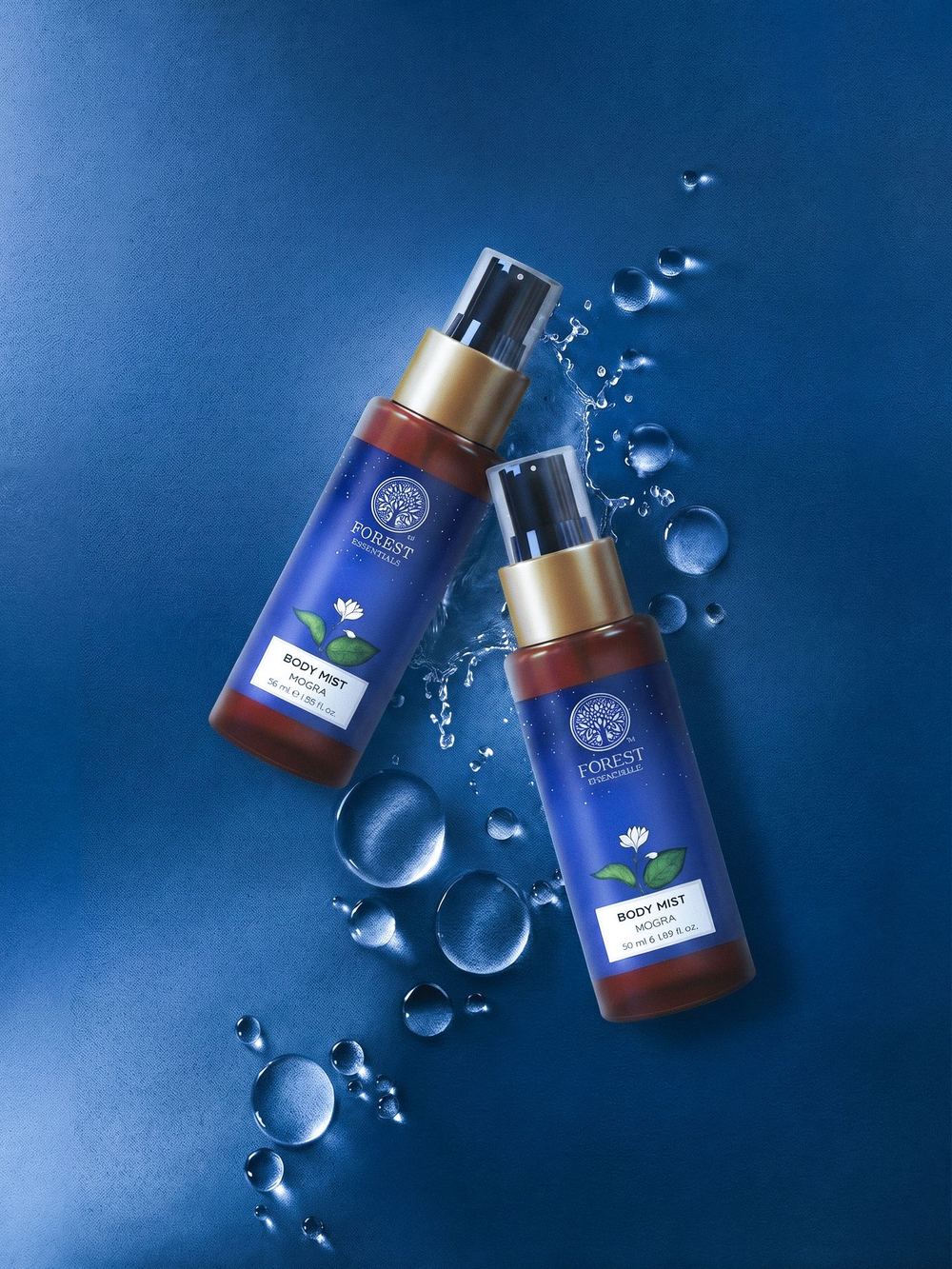 Two body-mist bottles on deep blue among water droplets.