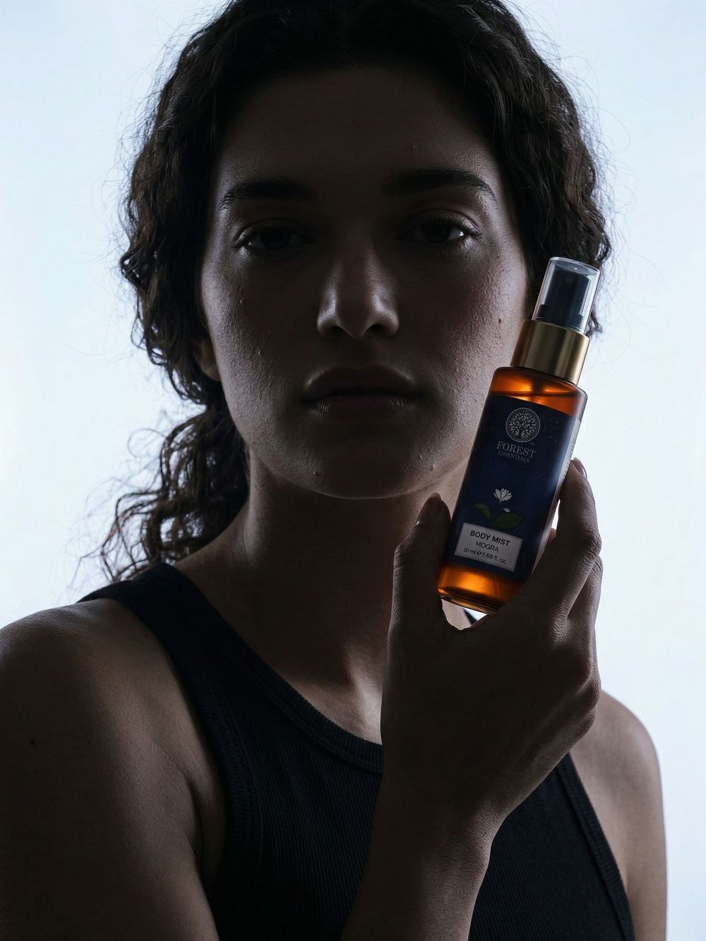 Holding a body-mist bottle beside the face in low light.