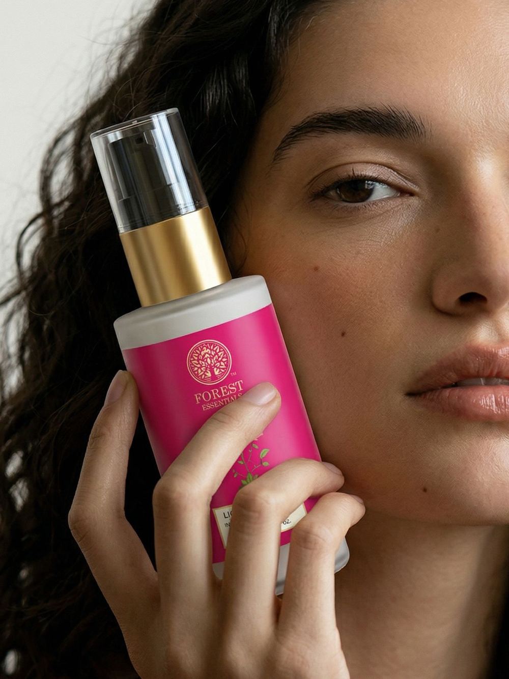 Close beauty frame with a pink body-mist bottle held to the cheek.