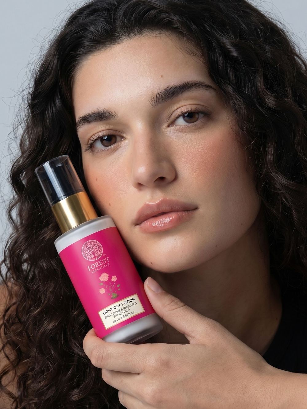 Beauty close-up with a pink bottle raised beside the face.