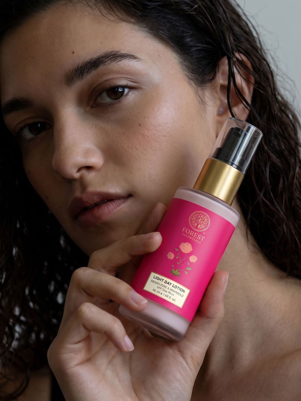 Portrait holding a pink body-mist bottle, hair in loose curls.