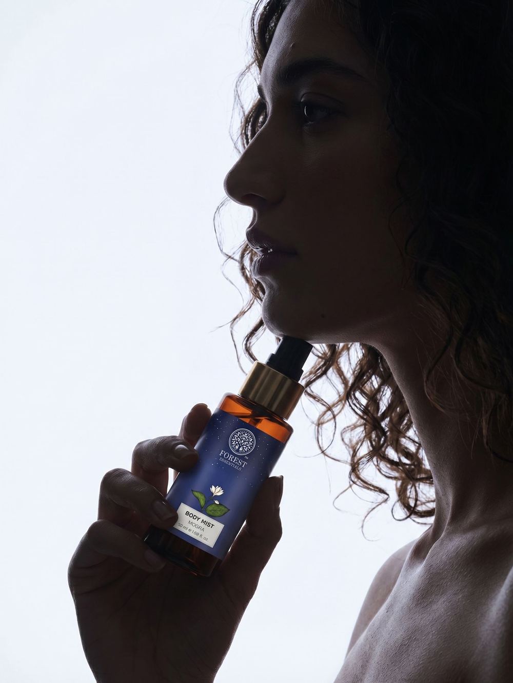 Profile frame holding a body-mist bottle up to the jaw.