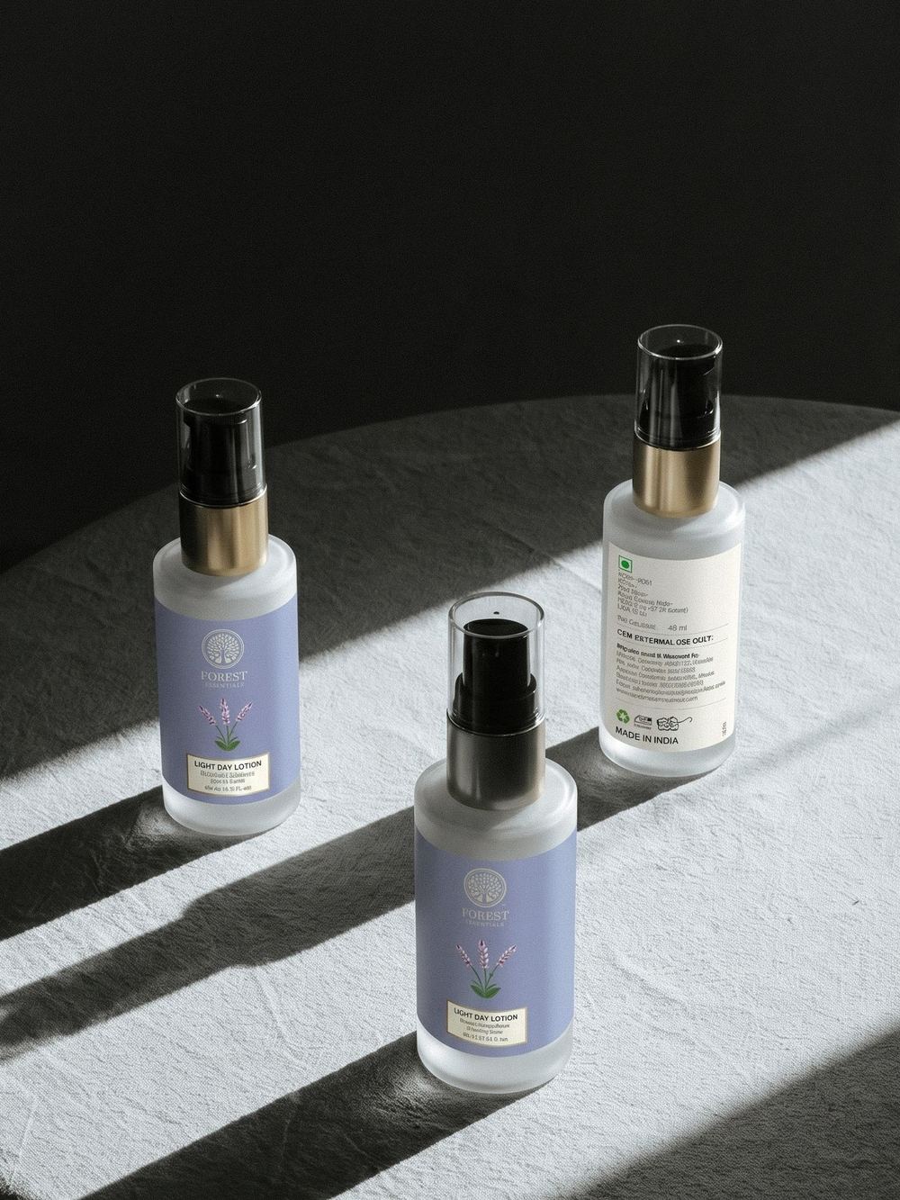 Three body-mist bottles on a pale ledge in hard diagonal light.