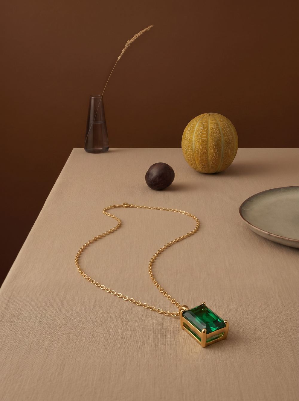 Emerald pendant necklace on a table with a vase and fruit.
