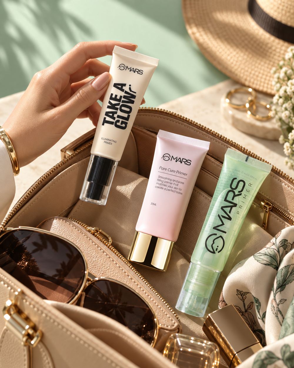 A hand lifting a MARS illuminating primer from an open tan vanity bag holding two more tubes, sunglasses and a sun hat alongside.