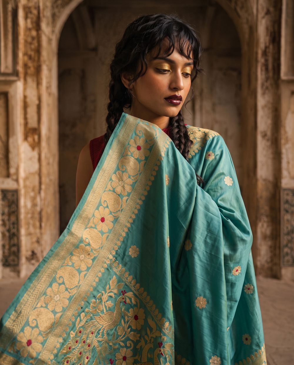 Close frame of a teal saree pallu with gold floral zari.