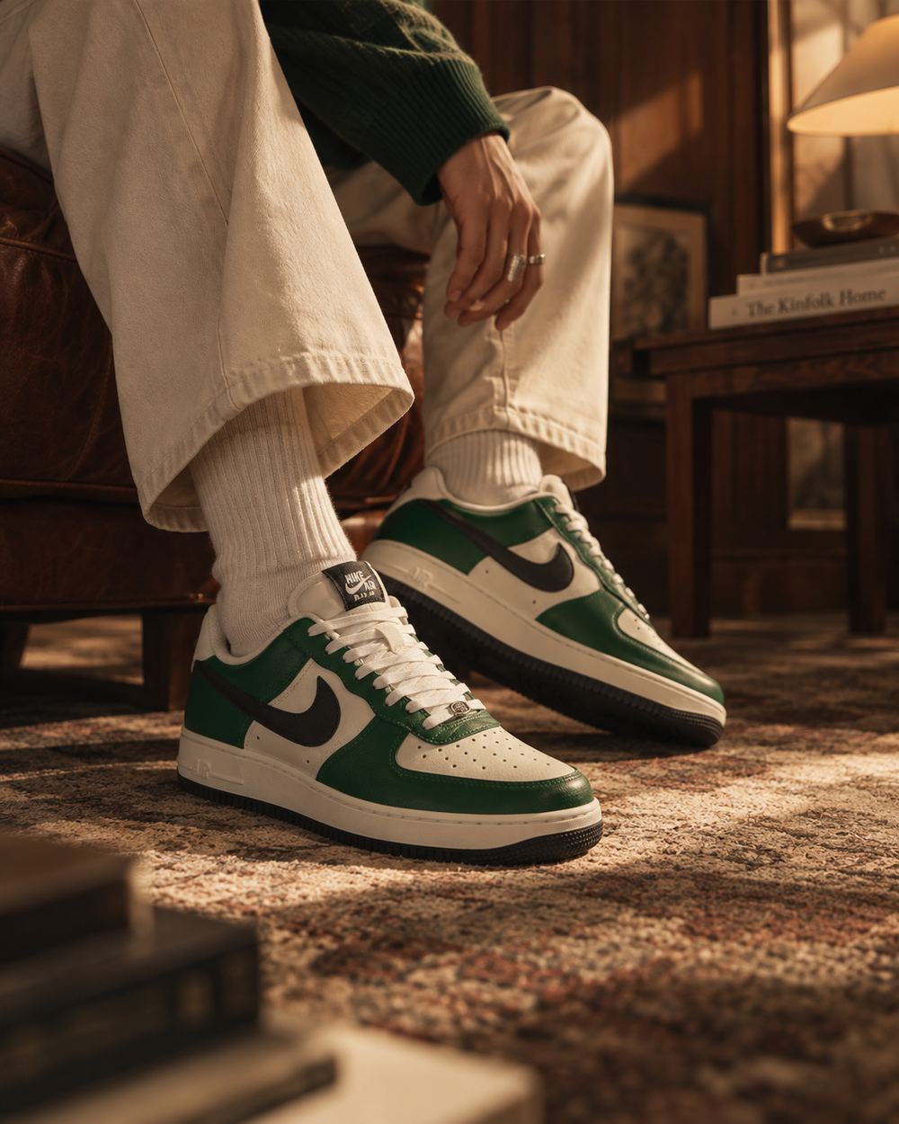 Close frame of the same green sneakers on crossed legs in cream trousers, late sun raking across the rug.