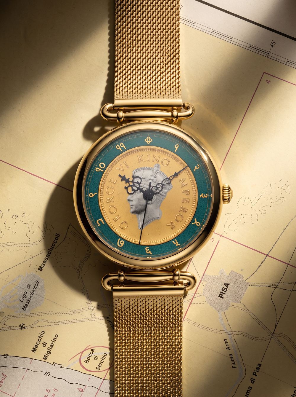 Gold coin watch on a map in warm raking light, shown at a three-quarter angle.