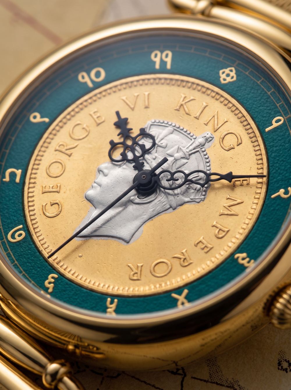 Macro of a gold coin watch dial, a monarch's profile struck into the coin inside a teal enamel ring.